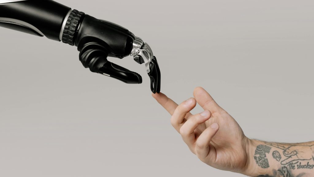 A human hand with tattoos reaching out to a robotic hand on a white background.